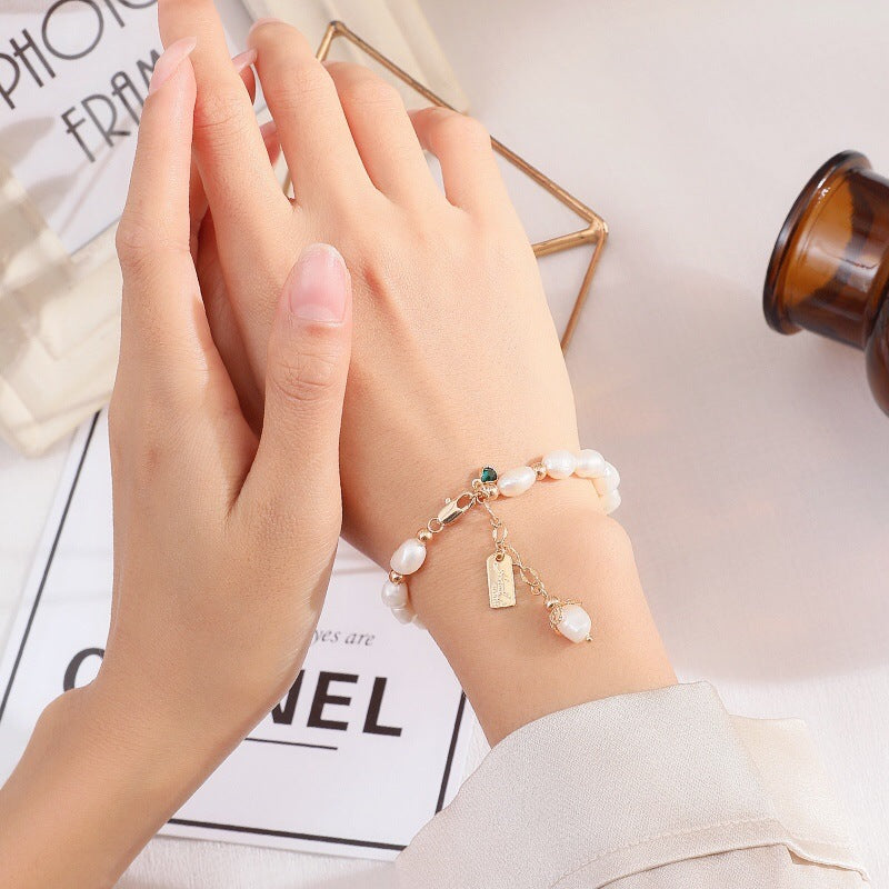 Elegantes Damenarmband mit natürlichen Perlen und goldfarbenen Anhängern am Handgelenk getragen – femininer Schmuck mit romantischer und luxuriöser Ausstrahlung
