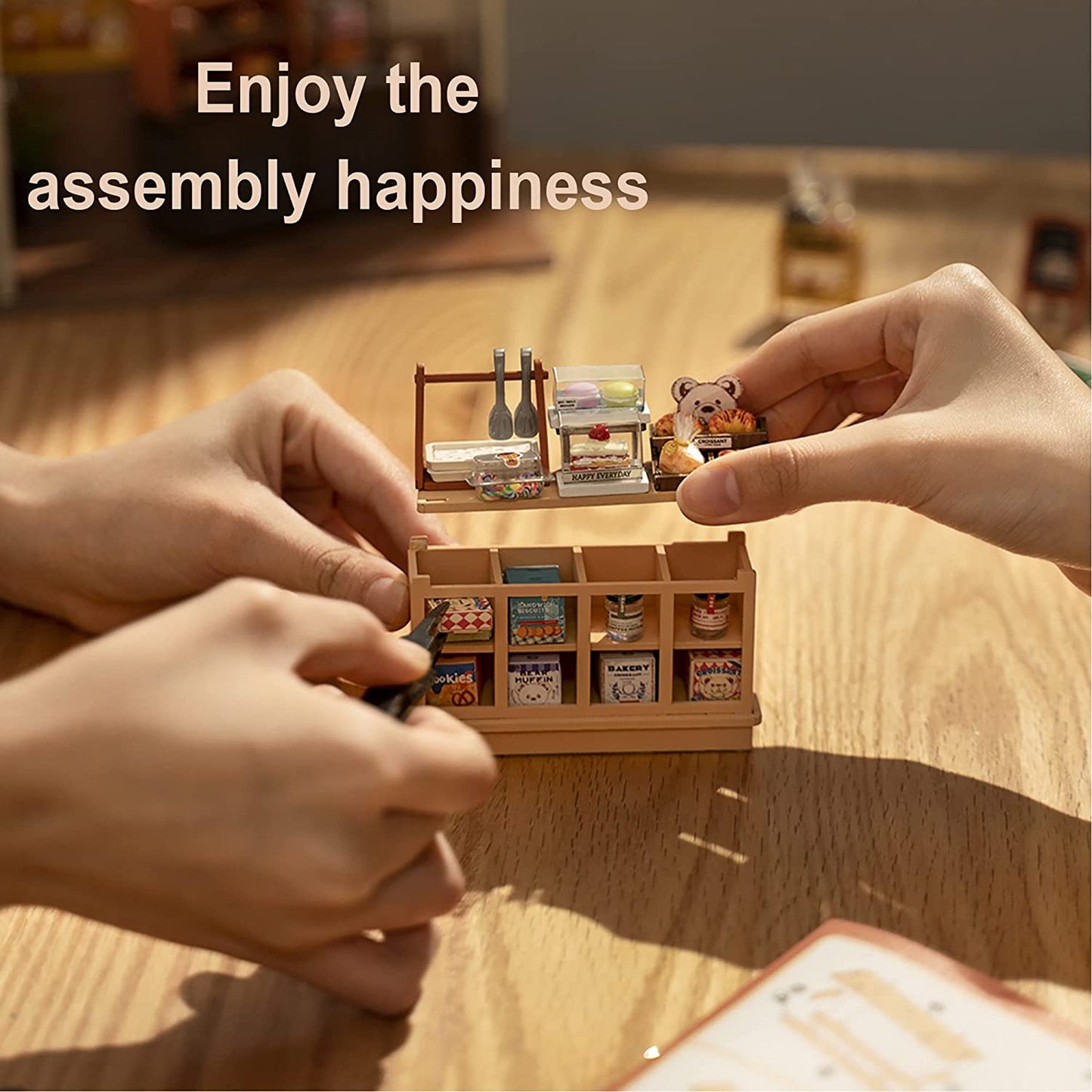 Hände beim Zusammenbauen eines detaillierten Miniatur-Bäckerei-DIY-Kits auf einem Holztisch – kreative Bastelszene mit gemütlicher Hobby-Atmosphäre