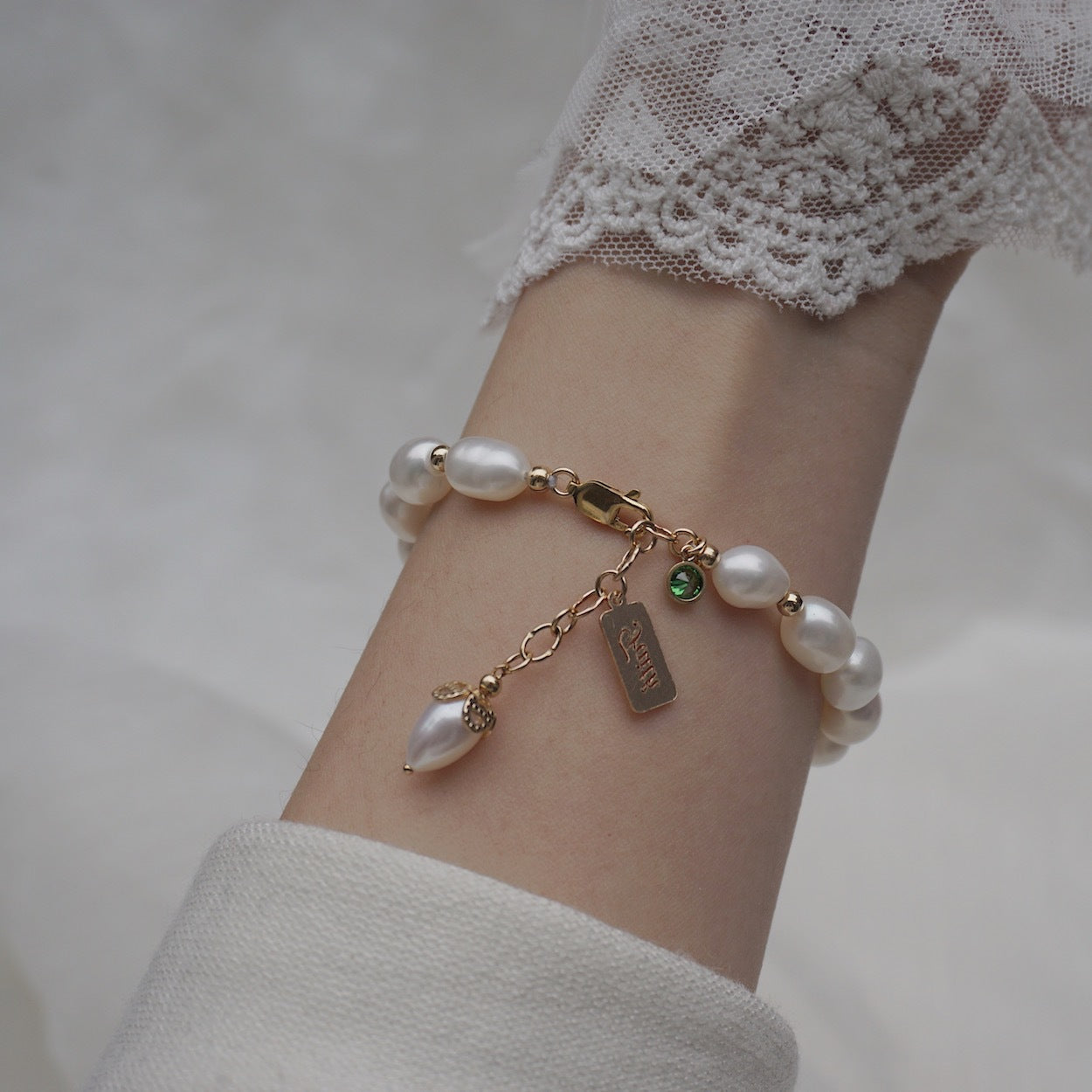 Elegantes Perlenarmband mit goldfarbenen Anhängern und natürlichen Perlen am Handgelenk getragen – femininer Damenschmuck mit romantischer Ausstrahlung