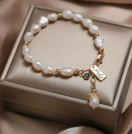 Elegantes Perlenarmband mit natürlichen Perlen, goldfarbenen Details und funkelndem Anhänger stilvoll auf einer Schmuckbox präsentiert